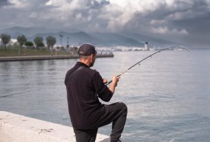 A man enjoys fishing on a cloudy day by the sea in İzmir, Türkiye.