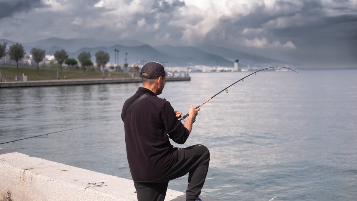A man enjoys fishing on a cloudy day by the sea in İzmir, Türkiye.